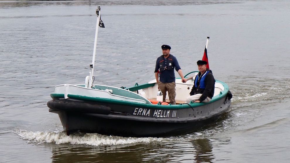 Das Festmacherboot Erna Hellm III fährt auf dem Wasser. An Bord befinden sich zwei Männer.