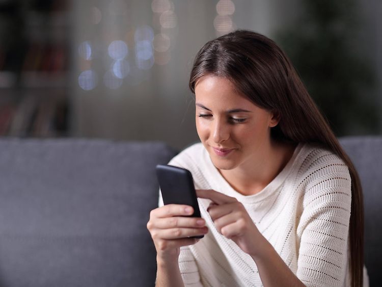  Eine Frau sitzt auf einem Sofa und scrollt durch ihr Smartphone.