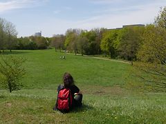  Frau sitzt auf Grashügel und schaut über Wiese.
