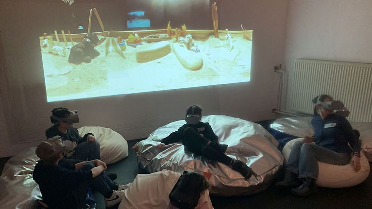  Mehrere Kinder mit 360-Grad-Kameras sitzen in einem Raum auf Sitzsäcken
