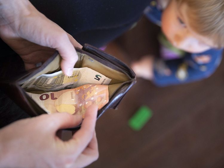  Ein Portemonnaie mit zwei Geldscheinen wird geöffnet und ein Kind ist im Hintergrund zu sehen.