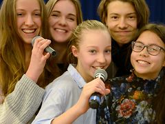  Jugendliche singen teilweise mit Mikrofon ausgestattet fröhlich lachend.