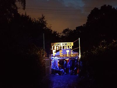  Ein Bild von einer Open Air Veranstaltung von "Keine Knete trotzdem Fete" im Gängeviertel. Zu sehen ist ein blau beleuchtetes Zelt mit einem goldenen Schild.
