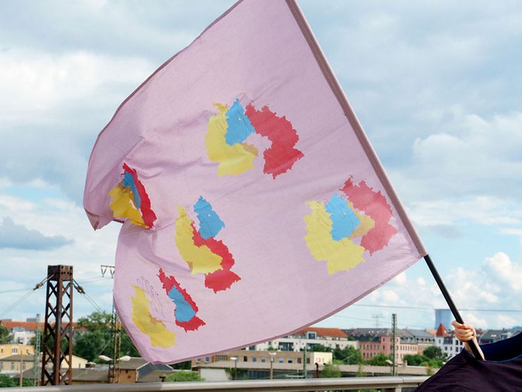  Eine große rosafarbene Flagge mit bunten Kontinenten und fein gezeichneten Händen.