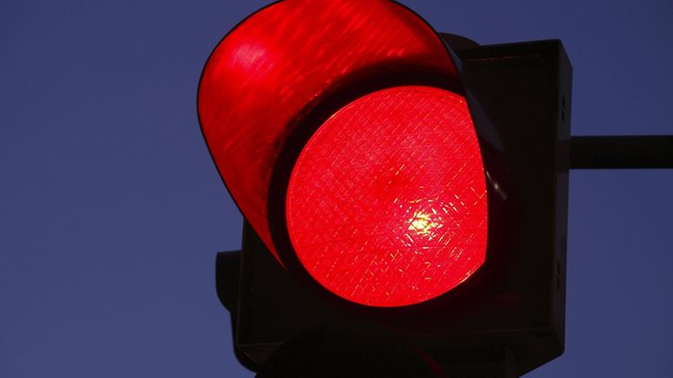  Das rote Licht einer Verkehrsampel in Großaufnahme vor einem dämmrigen, dunkelblauen Himmel.