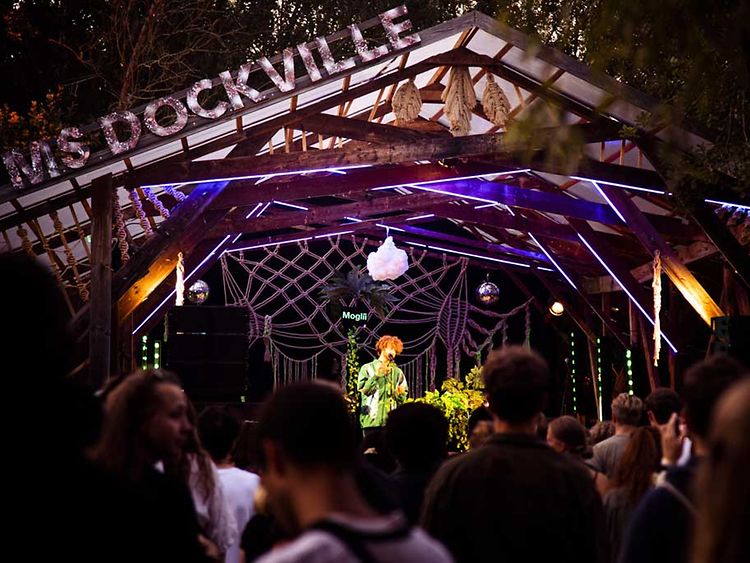  Die Bühne beim Fast ein MS Dockville Festival mit dem Musiker Moglii. Im Vordergrund sind ein paar BesucherInnen zu sehen. 