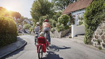  Zwei Personen fahren auf einer Straße jeweils auf einem Fahrrad. Sie tragen Helme. Die Sonne scheint.