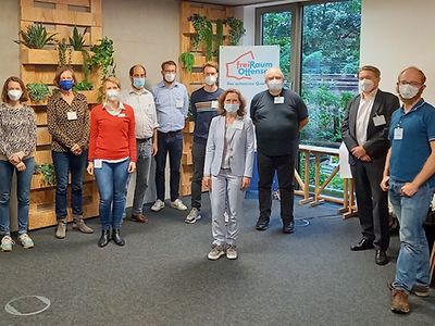  Eine Gruppe Menschen, die Masken tragen, stehen in einem Raum.