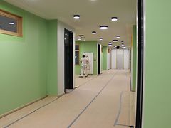  Ein langer Flur mit grünen Wänden, im Hintergrund arbeitet ein Maler. 