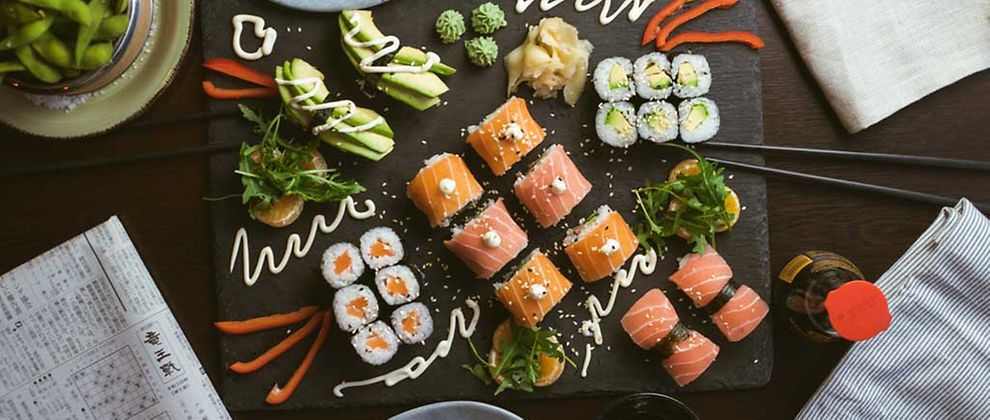  Eine Auswahl verschiedener Maki, Nigiri und Sashimi Sushi mit Fisch und Avocado verziert mit Saucen, Wasabi und Ingwer, Sesam.