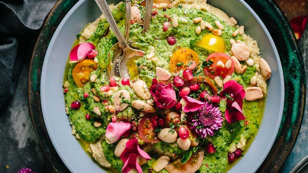  Eine vegane Bowl aus grüner Creme mit Mandeln und rosa Blüten dekoriert