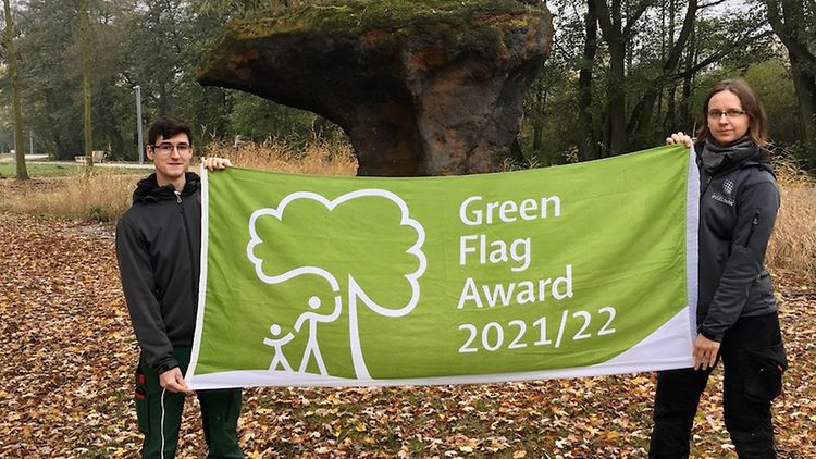  Zwei Personen halten einen grünen Banner mit Beschriftung in einem Park.