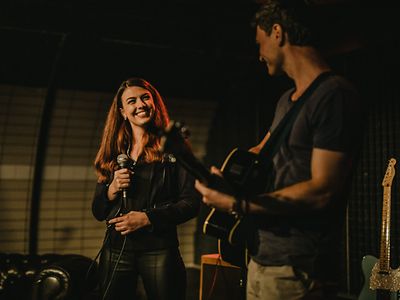  Eine Sängerin und ein Gitarrist lächeln sich an.