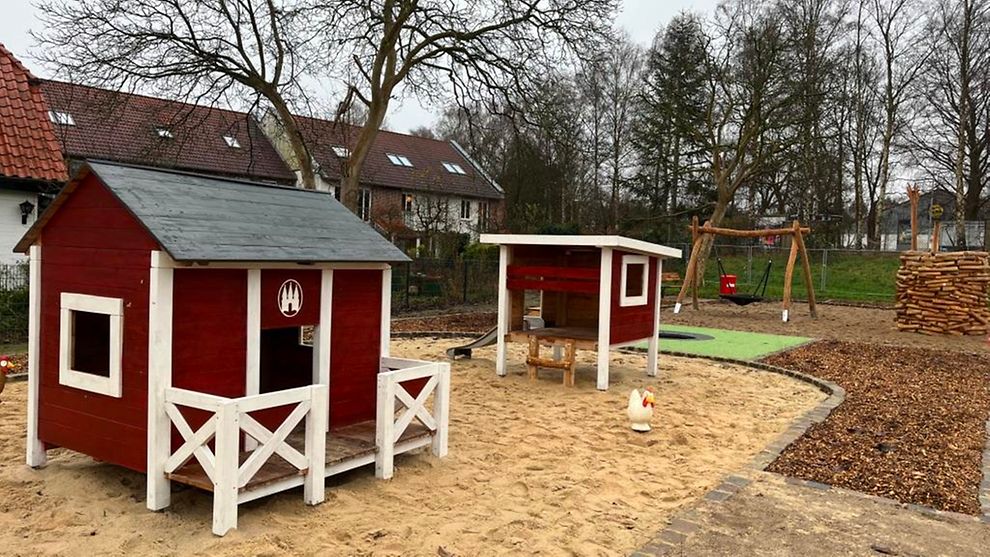 Zwei kleine Häuser stehen in einem Sandkasten eines Spielplatzes.