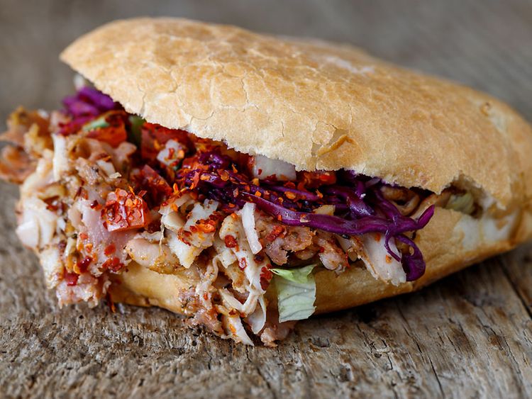  Ein Döner Sandwich mit Chili, Fleisch, Salat und Rotkohl auf Holzuntergrund.