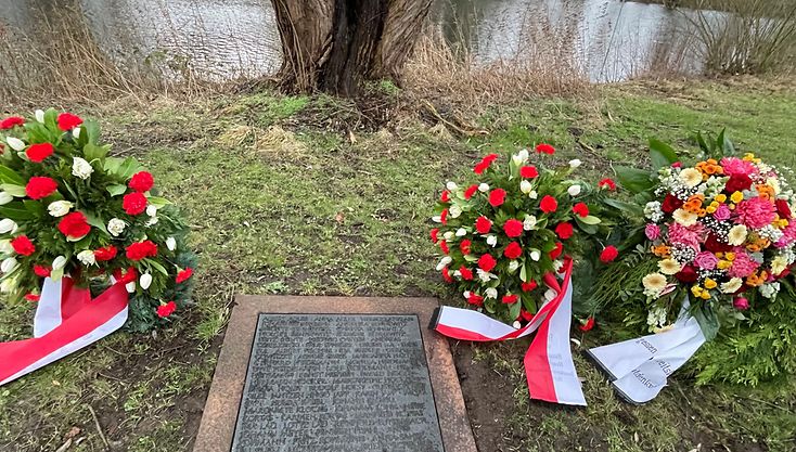 Eine Aufnahme einer Gedenktafel mit den Namen von Verstorbenen sowie mehrere Blumenkränze.