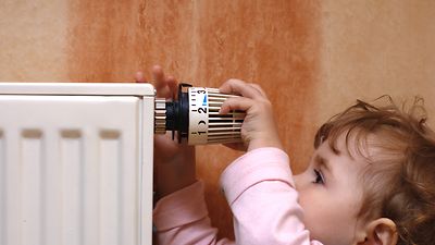  Kleines Kind dreht am Thermostat einer Heizung
