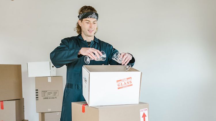 Ein Mensch packt Gläser in Kisten ein