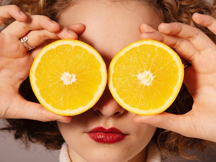  Eine Frau hält sich je eine Hälfte einer Orange vor die Augen