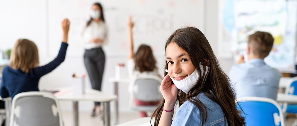 Eine Schülerin sitzt im Klassenzimmer, ihre Maske trägt sie auf Kinnhöhe 