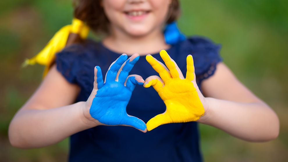 Das Bild zeigt ein Kind, das seine Handflächen zeigt. Die eine ist blau, die andere gelb ind den Farben der Ukraine bemalt.