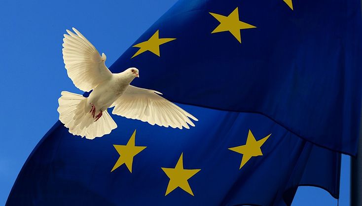 Eine weiße Taube fliegt vor einer Europaflagge.