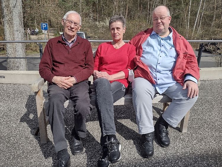  Drei Personen sitzen auf einer Bank.
