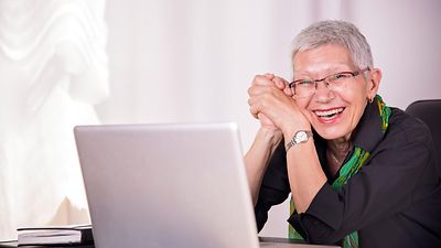  Ältere Dame lacht hinter einem Notebook