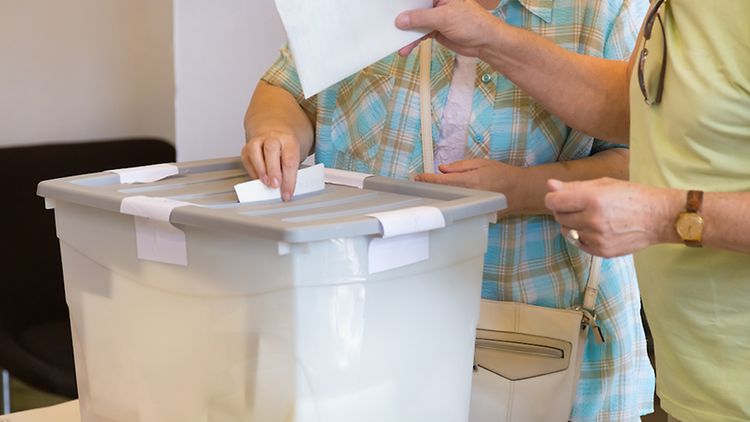  Ältere Personen werfen Stimmzettel in eine Wahlurne