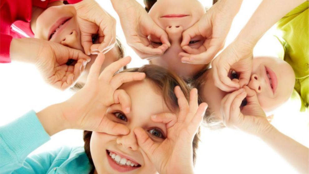 Kinder formen ihre Hände zu Augen und schauen durch die Löcher in eine Kamera.