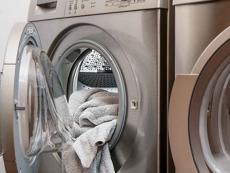  Offene Waschmaschinentür aus der ein Handtuch hängt.