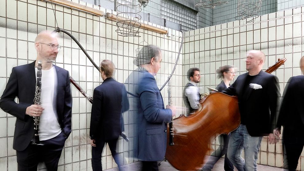  Schwarz-weiß gekleidete Menschen stehen in einer Reihe und halten klassische Musikinstrumente. 
