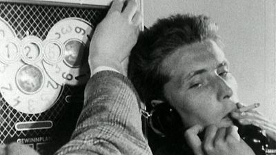  Filmstill: Mann zeiht an einer Zigarette und hat einen Telefonhörer in der Hand