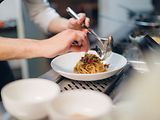  Ein Koch richtet auf einem weißen Teller eine Portion Spaghetti an.