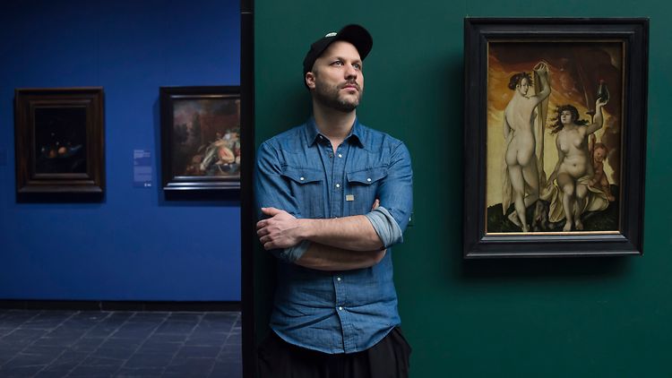  Tobias Kratzer steht vor einer Wand mit Kunstwerken