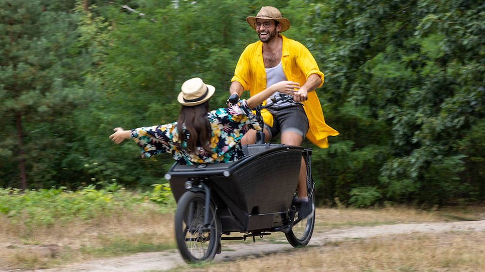 Ein Mann fährt Lastenrad mit einem Kind