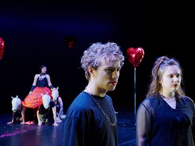  Jugendliche mit aufgemaltem Bart und rotem Lippenstift stehen auf einer Bühne.