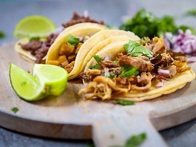  Auf einem Holzbrett liegen gefüllte Tacos und aufgeschnittene Limetten.