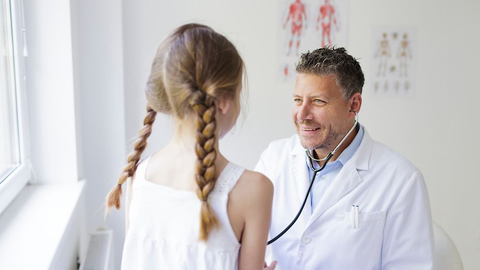 Ein Arzt hört ein Mädchen mit einem Stethoskop ab.