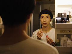  Ein Mann betrachtet ernst sein Spiegelbild und trägt sich Lippenstift auf.