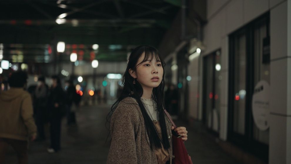  Eine Frau schaut in die Ferne. Im Hintergrund sieht man eine japanische Bahnstation.