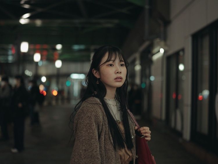 Eine Frau schaut in die Ferne. Im Hintergrund sieht man eine japanische Bahnstation.