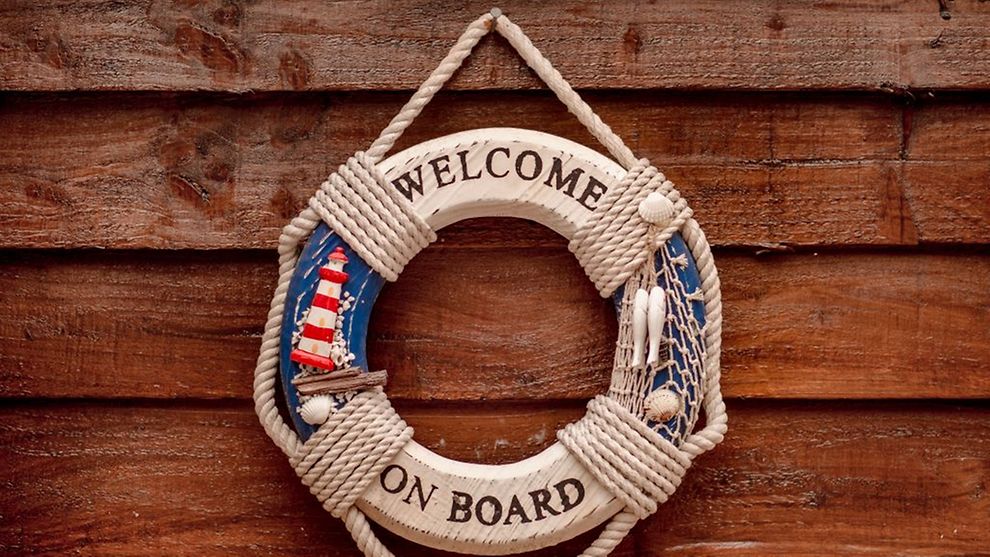  An einer Holzwand hängt ein Rettungsring mit der Aufschrift Welcome on board.