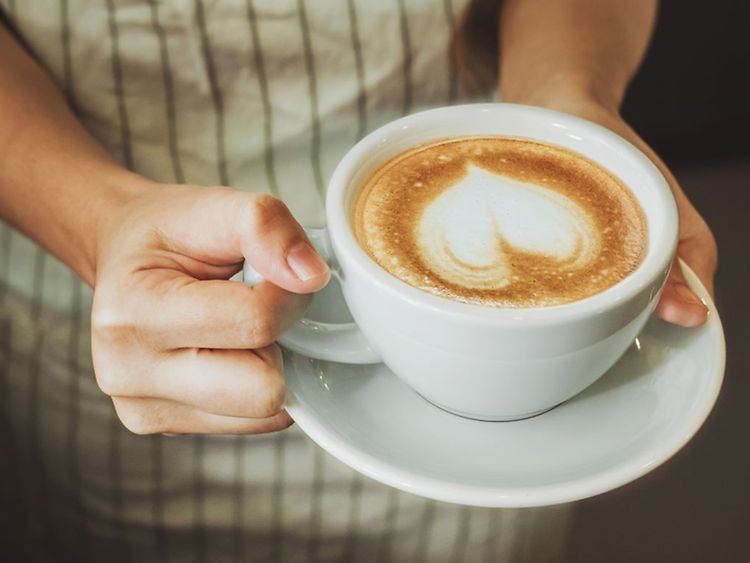  Eine Frau hält eine Tasse Kaffee mit einem Herz aus Milchschaum.