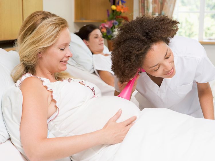  Eine Krankenschwester horcht am Bauch einer Schwangeren