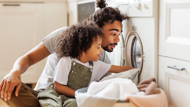 Ein Mann und ein Kind schauen in eine geöffnete Waschmaschine und entleeren diese.