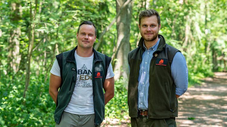  Die zwei neuen Kollegen stehen auf einem Waldweg im Hamburger Klövensteen.