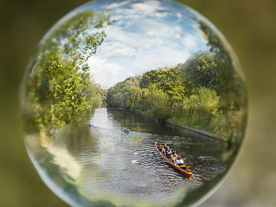  Glaskugel, in der ein Kanal und Bäume abgebildet sind. Auf dem Wasser fährt ein Ruderboot.