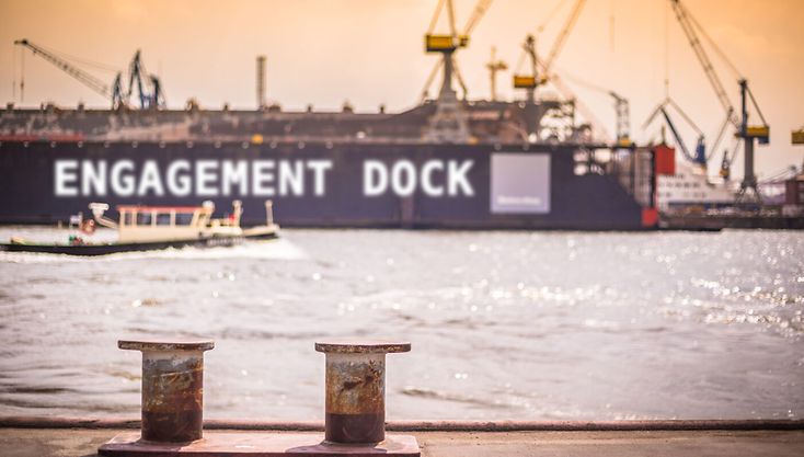 Das Bild zeigt ein motiv aus dem Hamburger Hafen: im Vordergrund zwei Festmacherpoller, auf der anderen Uferseite liegt ein großes Trockendock mit der Aufschrift: 
