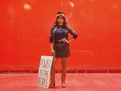  Foto einer trans*Frau, an deren Bein ein Schild mit der Aufschrift "Power to the People" lehnt.